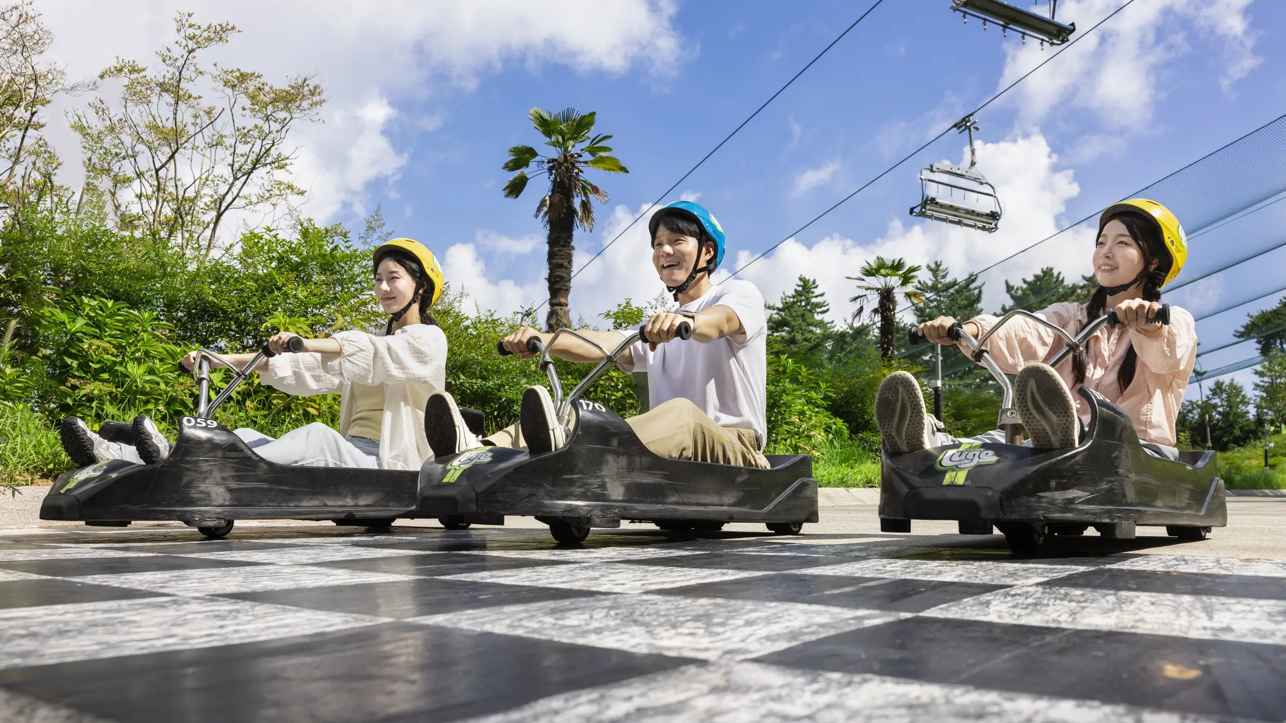 Riders crossing the finish line at Skyline Luge Tongyeong on a sunny day.