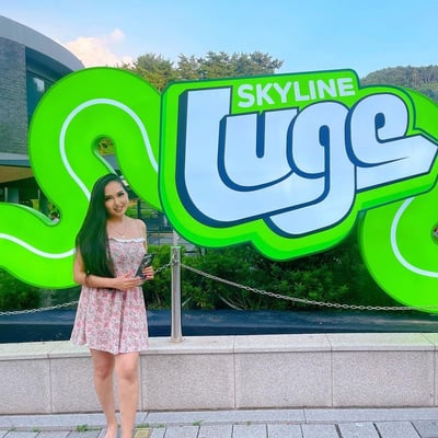 A lady poses in front of the big neon Luge sign.