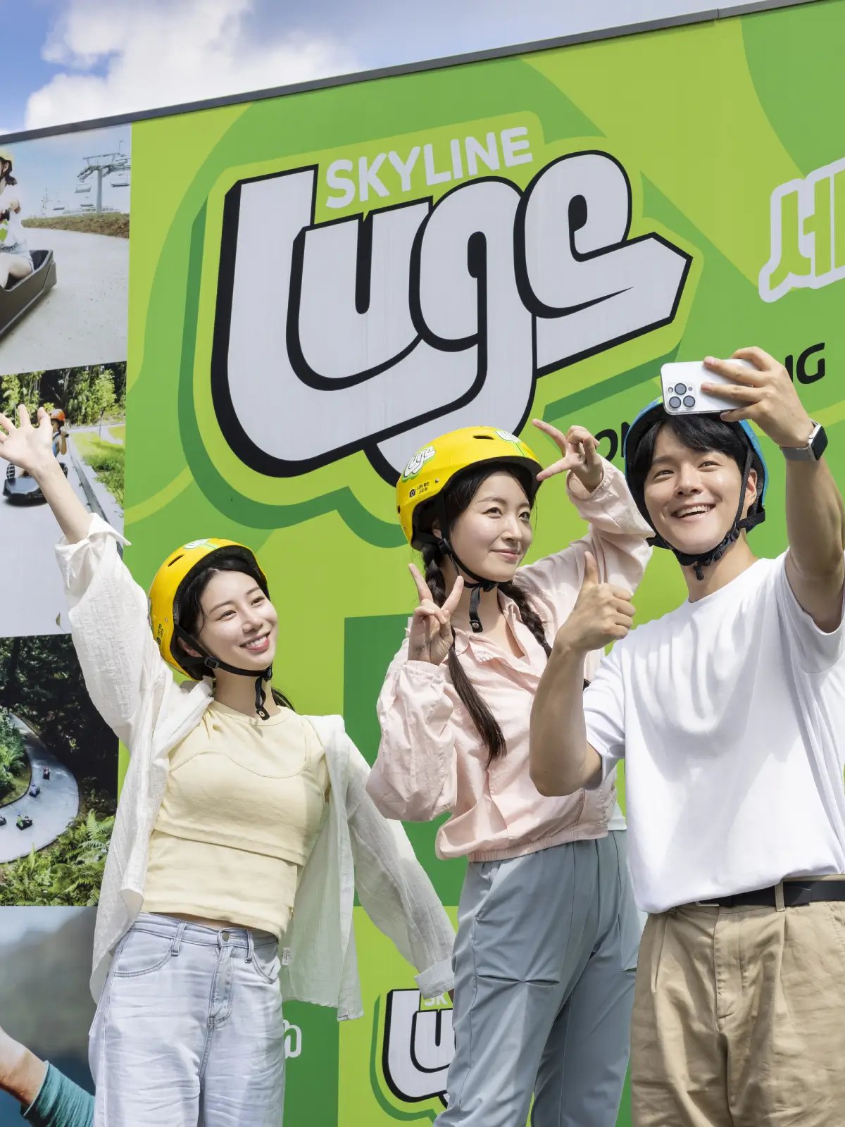 isitors taking a selfie in front of the Skyline Luge Tongyeong photo wall.