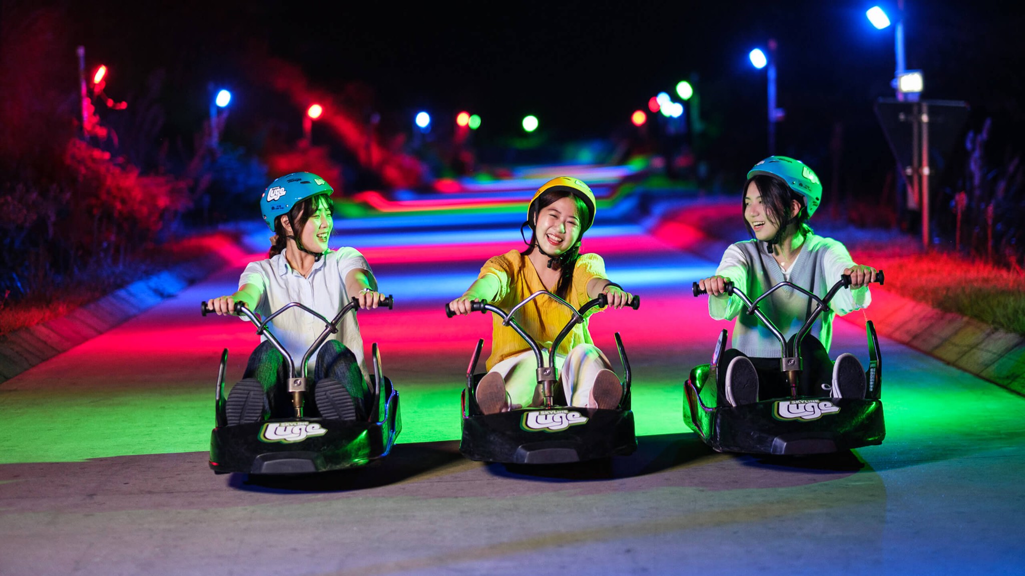 Three women ride the colourful Night Luge tracks together.