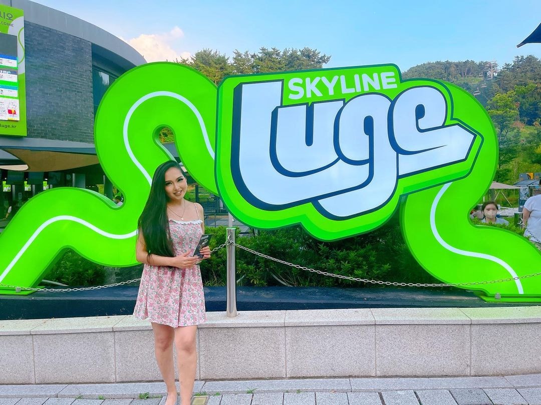 A lady poses in front of the big neon Luge sign.