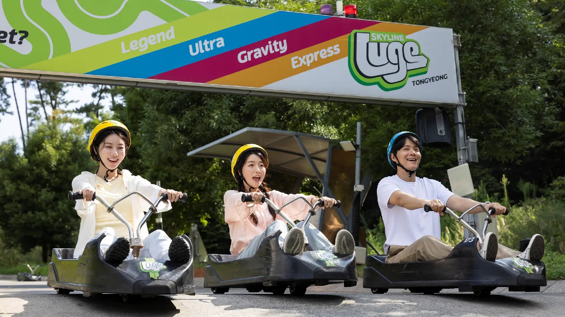 Riders enjoying a downhill run at Skyline Luge Tongyeong under the track signage.